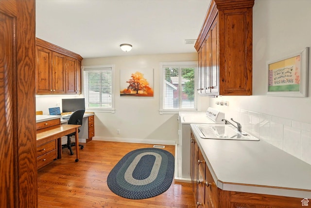 home office featuring light wood-type flooring, washer and dryer, baseboards, and a sink
