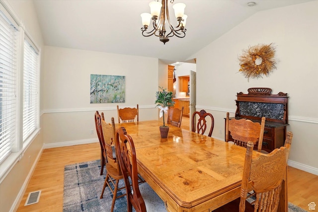 dining room featuring light wood-style flooring, vaulted ceiling, a chandelier, plenty of natural light, and baseboards