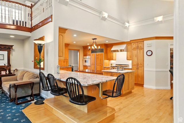 kitchen featuring white oven, a towering ceiling, wall chimney range hood, a peninsula, and a chandelier