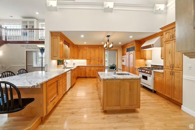kitchen featuring white appliances, wall chimney exhaust hood, a sink, a chandelier, and plenty of natural light