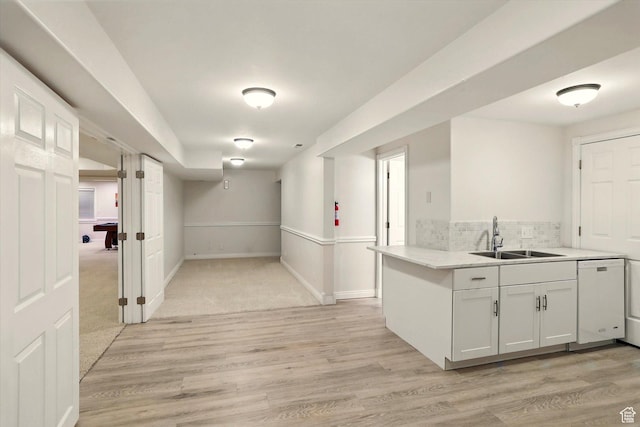 kitchen featuring a sink, white dishwasher, light wood finished floors, backsplash, and white cabinetry