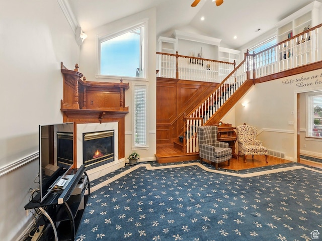 living area with high vaulted ceiling, ceiling fan, plenty of natural light, stairs, and a high end fireplace