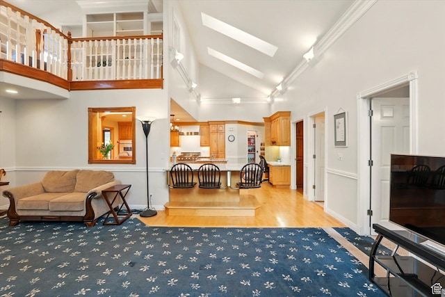 living area with a skylight, light wood finished floors, high vaulted ceiling, and baseboards