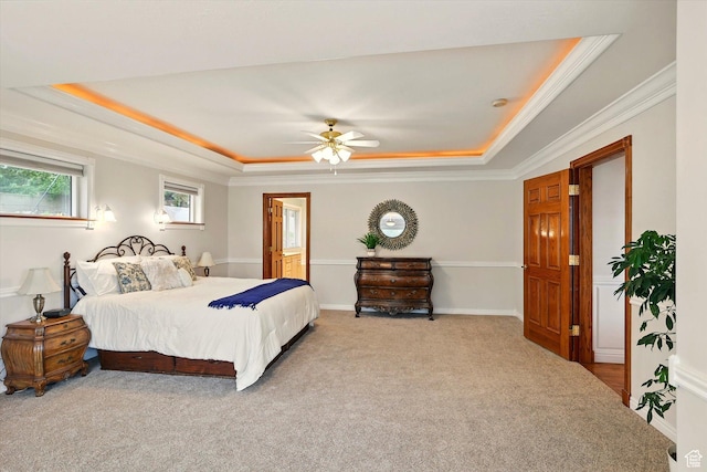 bedroom with a tray ceiling, carpet flooring, ornamental molding, ensuite bath, and ceiling fan