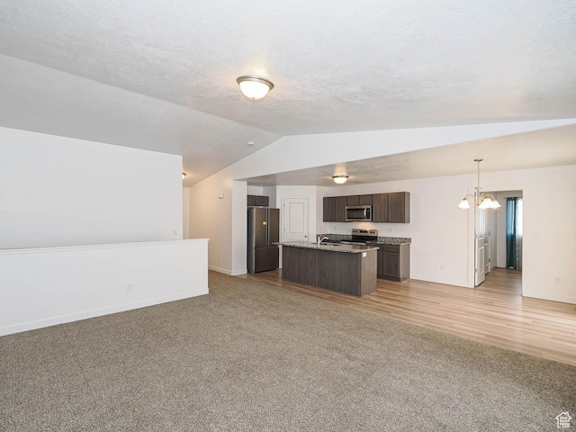 kitchen with open floor plan, stainless steel appliances, vaulted ceiling, dark brown cabinetry, and light carpet