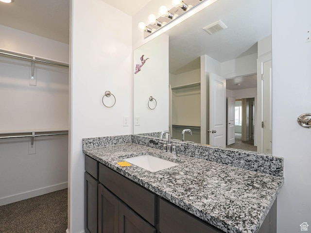 bathroom with a walk in closet, vanity, and baseboards