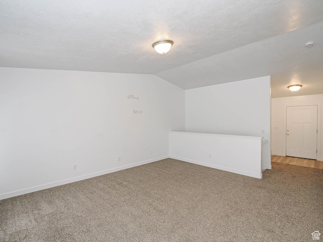 additional living space with carpet flooring, a textured ceiling, vaulted ceiling, and baseboards