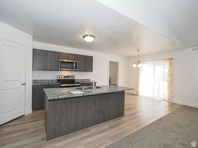 kitchen featuring stainless steel appliances, a sink, a chandelier, light stone counters, and light wood finished floors