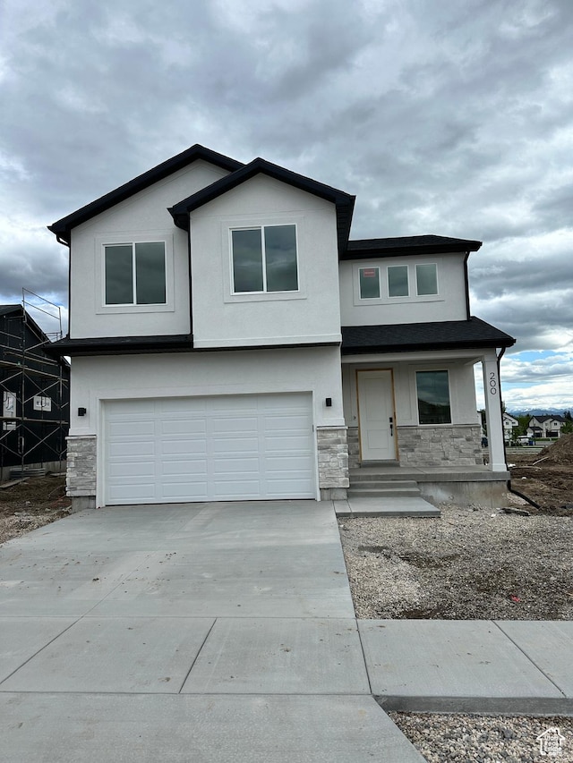 view of front of home with a garage, stone siding, concrete driveway, stucco siding, and a porch