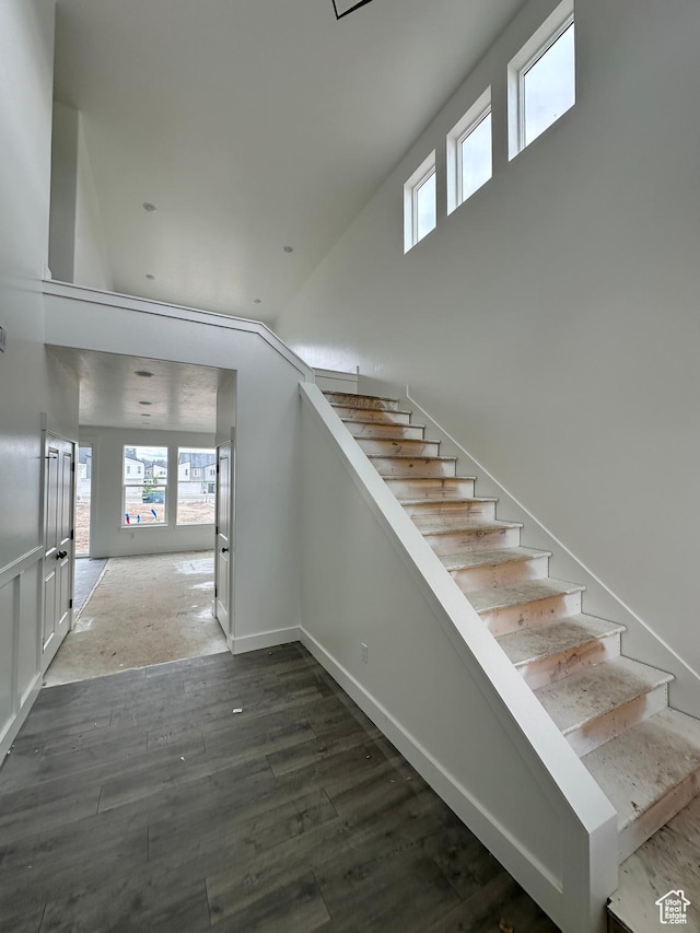 stairway with wood finished floors and a towering ceiling