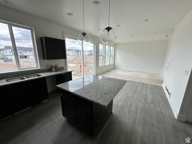 kitchen with dark cabinets, a sink, wood finished floors, light stone counters, and pendant lighting