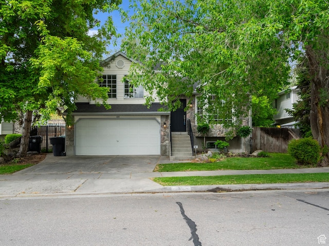 view of front facade featuring fence, driveway, a garage, and stone siding