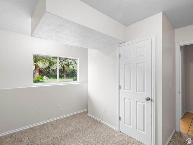 unfurnished bedroom with baseboards, a textured ceiling, and light carpet