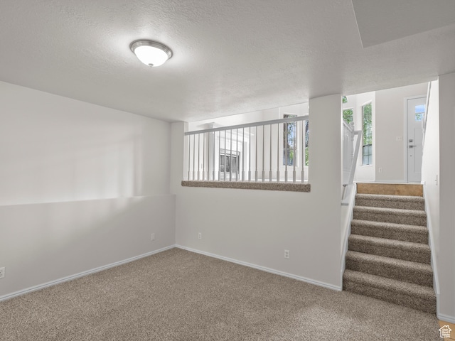 spare room featuring carpet, a textured ceiling, baseboards, and stairs