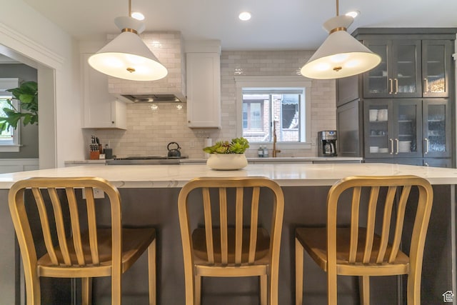 158 N State St, Salt Lake City, UT 84103 - kitchen with decorative backsplash, glass insert cabinets, white cabinetry, light stone countertops, and pendant lighting