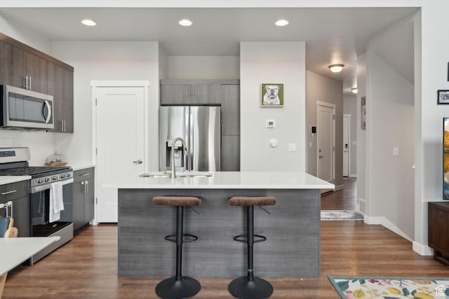 kitchen with appliances with stainless steel finishes, a sink, a kitchen bar, a kitchen island with sink, and light countertops