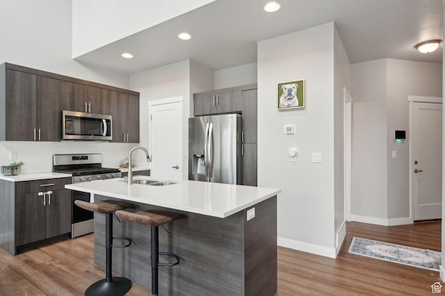 kitchen featuring appliances with stainless steel finishes, a sink, a breakfast bar area, light countertops, and wood finished floors