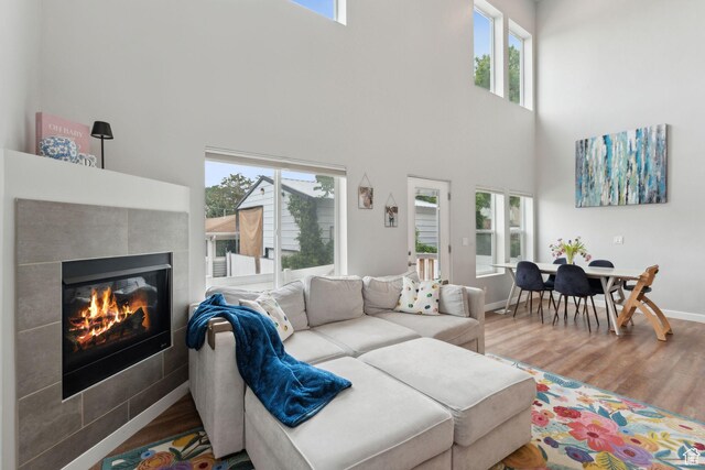 living room featuring wood finished floors, a high ceiling, plenty of natural light, a tile fireplace, and baseboards