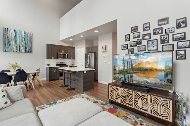 living room with wood finished floors, baseboards, recessed lighting, and a towering ceiling