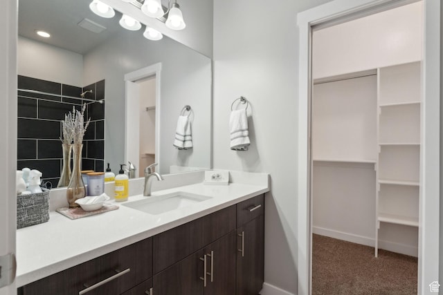 full bathroom featuring a walk in closet, a tile shower, vanity, and baseboards