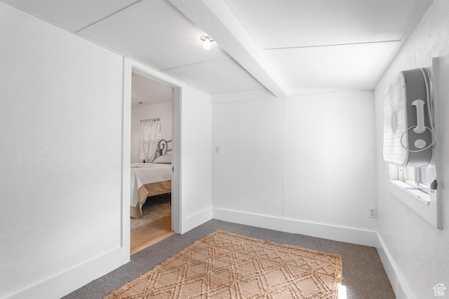 spare room featuring carpet floors, baseboards, and beamed ceiling