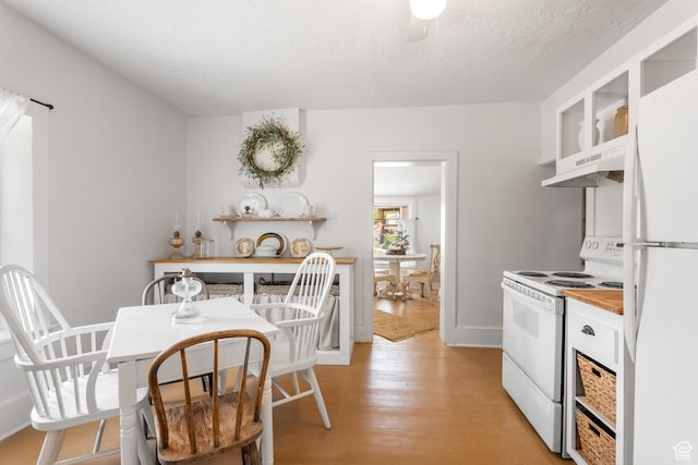 kitchen featuring white appliances, under cabinet range hood, white cabinets, light wood-style flooring, and glass insert cabinets