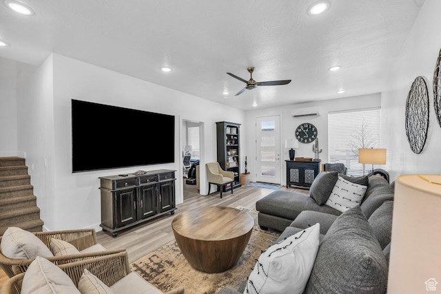 living area featuring a wall mounted air conditioner, recessed lighting, light wood finished floors, ceiling fan, and stairs