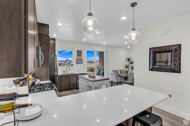 kitchen featuring dark brown cabinetry, light wood finished floors, light countertops, a breakfast bar, and a sink