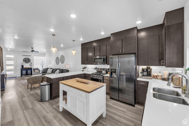 kitchen featuring appliances with stainless steel finishes, a sink, wood counters, open floor plan, and dark brown cabinets