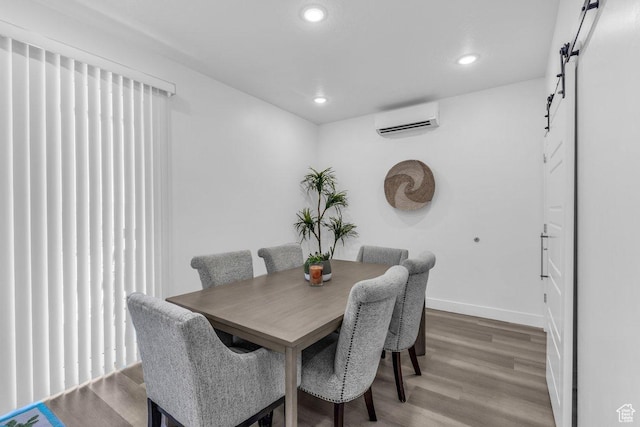 dining space featuring a wall unit AC, a barn door, light wood-type flooring, baseboards, and recessed lighting