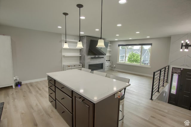 kitchen with baseboards, a kitchen island, light wood-style floors, light countertops, and a large fireplace
