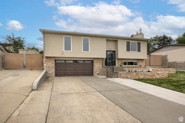 bi-level home featuring a garage, fence, concrete driveway, and a chimney