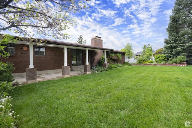 back of house with a chimney, a lawn, and brick siding
