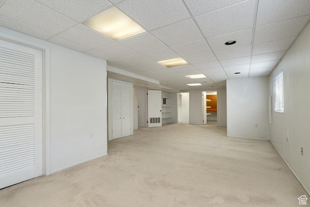 basement with a paneled ceiling, light carpet, and baseboards