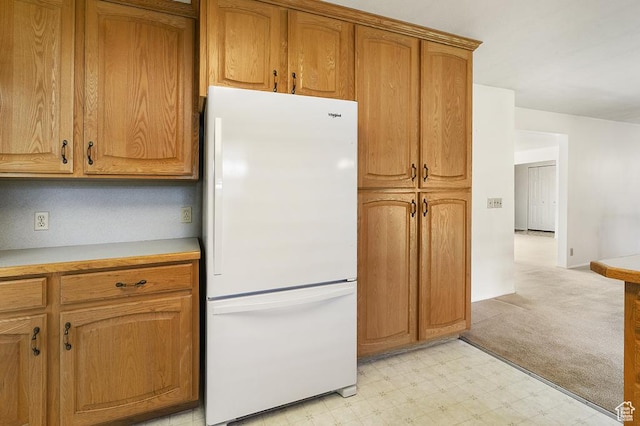 kitchen featuring freestanding refrigerator, light flooring, brown cabinetry, and light countertops