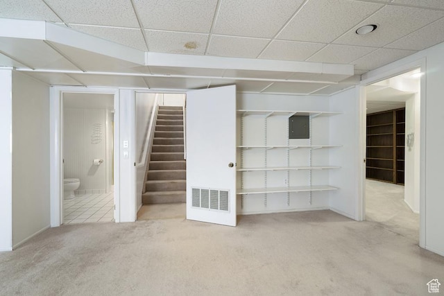 finished basement featuring carpet, electric panel, stairway, and a paneled ceiling