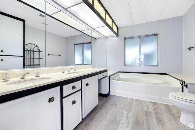 full bathroom featuring wood finished floors, a bath, double vanity, and toilet