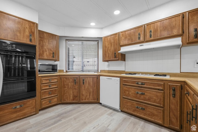 kitchen featuring white appliances, under cabinet range hood, a sink, brown cabinets, and decorative backsplash