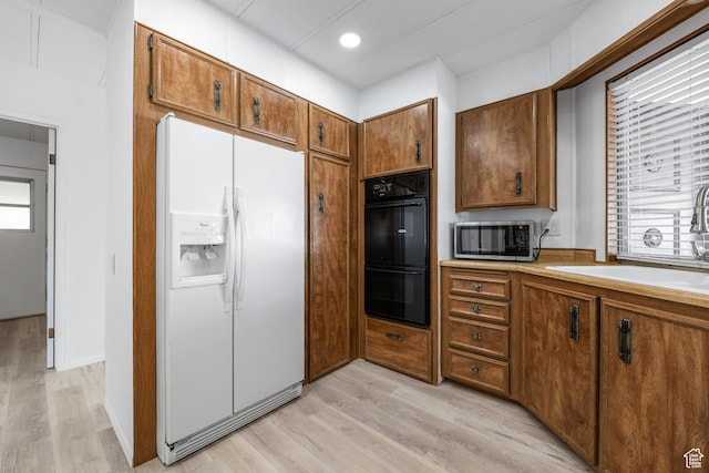 kitchen with white fridge with ice dispenser, stainless steel microwave, a sink, brown cabinets, and light wood-style flooring