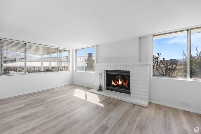 unfurnished living room featuring a brick fireplace, wood finished floors, healthy amount of natural light, and baseboards