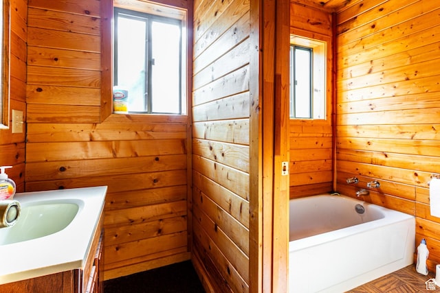 full bath featuring wood walls, plenty of natural light, a tub, and vanity