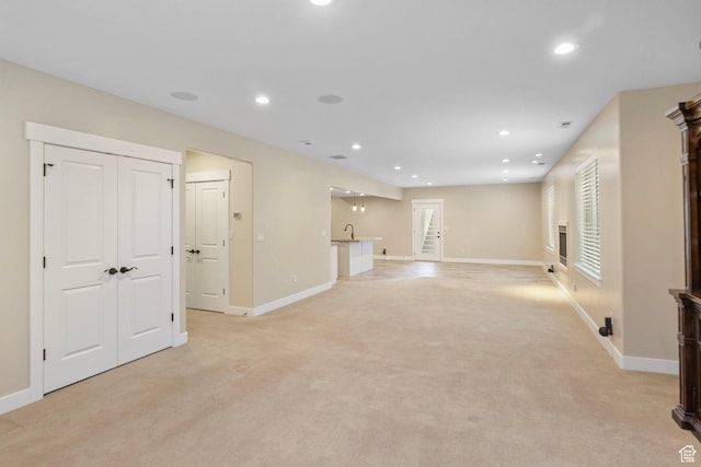 unfurnished living room with baseboards, recessed lighting, light colored carpet, and a sink