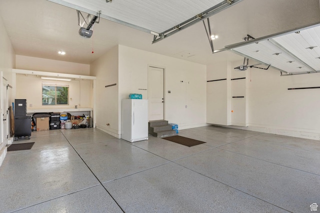 garage with a garage door opener, freestanding refrigerator, and baseboards