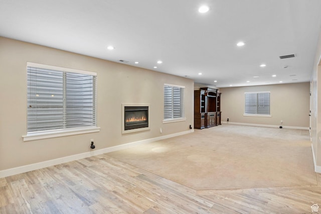 unfurnished living room with a glass covered fireplace, baseboards, recessed lighting, and light wood-type flooring