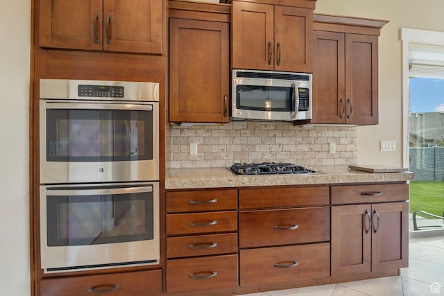 kitchen featuring stainless steel appliances, backsplash, brown cabinetry, and light tile patterned floors