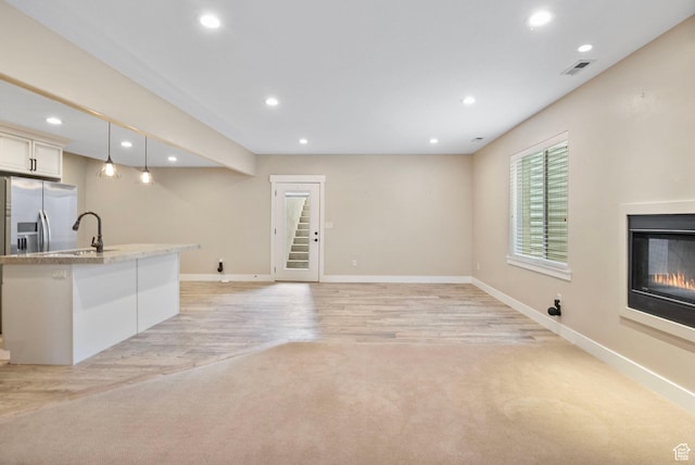unfurnished living room with recessed lighting, baseboards, a sink, a glass covered fireplace, and light wood-style floors