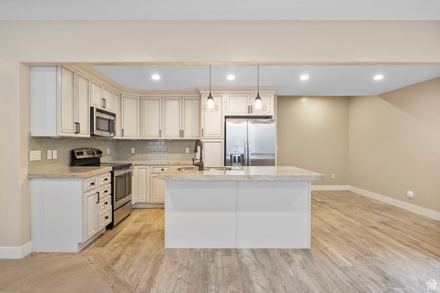 kitchen with appliances with stainless steel finishes, an island with sink, baseboards, a sink, and tasteful backsplash