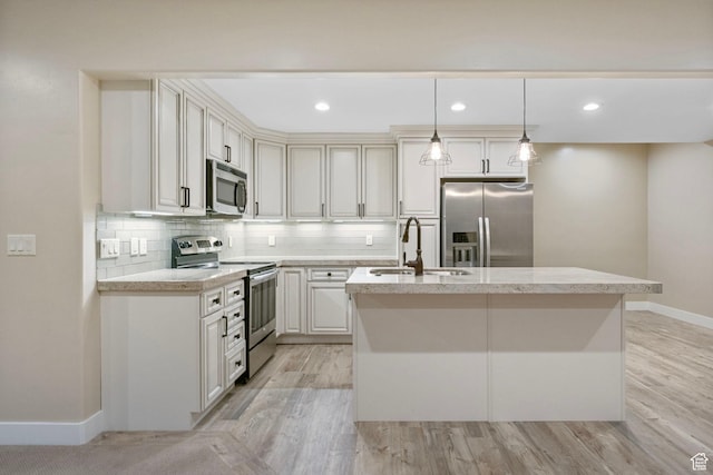 kitchen with appliances with stainless steel finishes, a sink, a kitchen island with sink, baseboards, and decorative backsplash