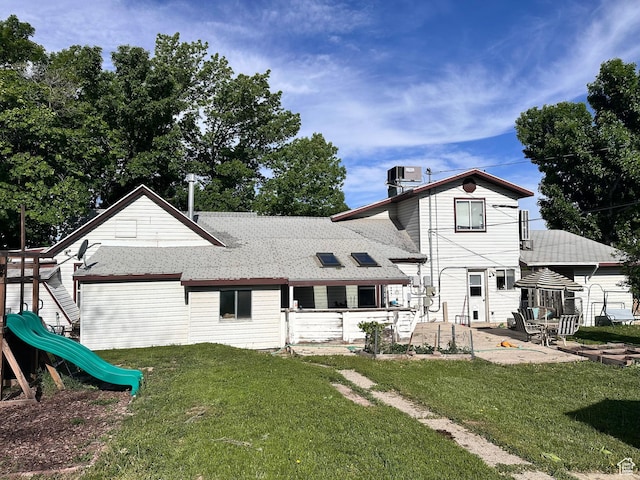 rear view of house featuring a patio area, a playground, a lawn, and roof with shingles