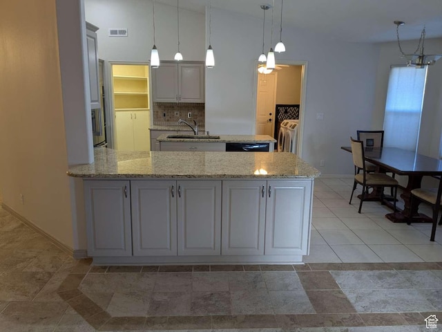 kitchen featuring a sink, washing machine and clothes dryer, a peninsula, decorative backsplash, and light stone countertops